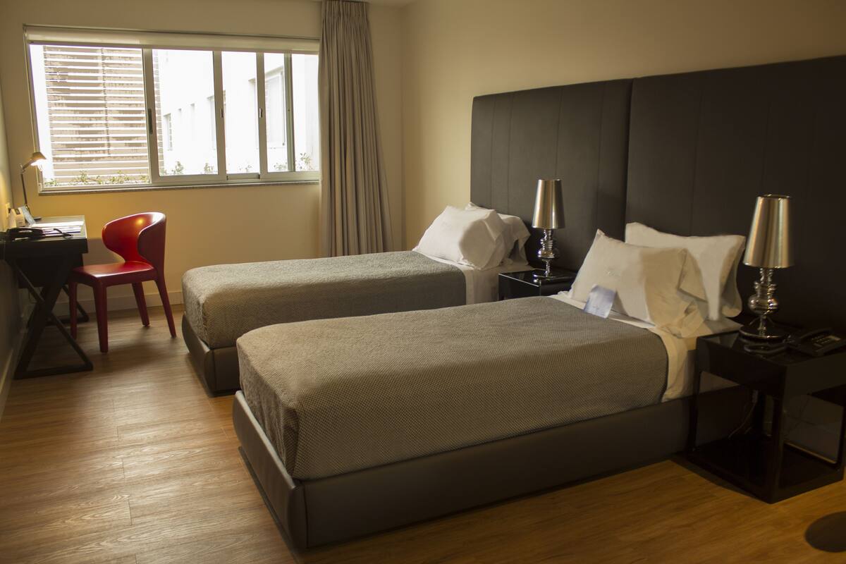 Habitación de hotel con dos camas, un escritorio, una silla y una ventana con persianas.