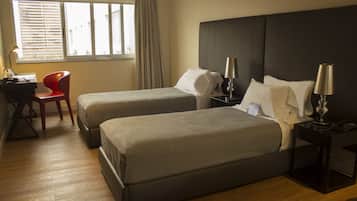 A hotel room with two beds, a desk, a chair, and a window with blinds.