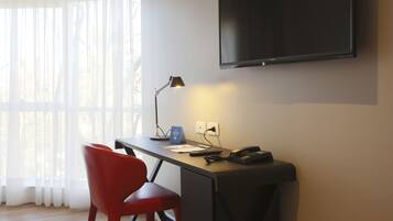 A modern office space with a desk, chair, lamp, and a mounted TV.