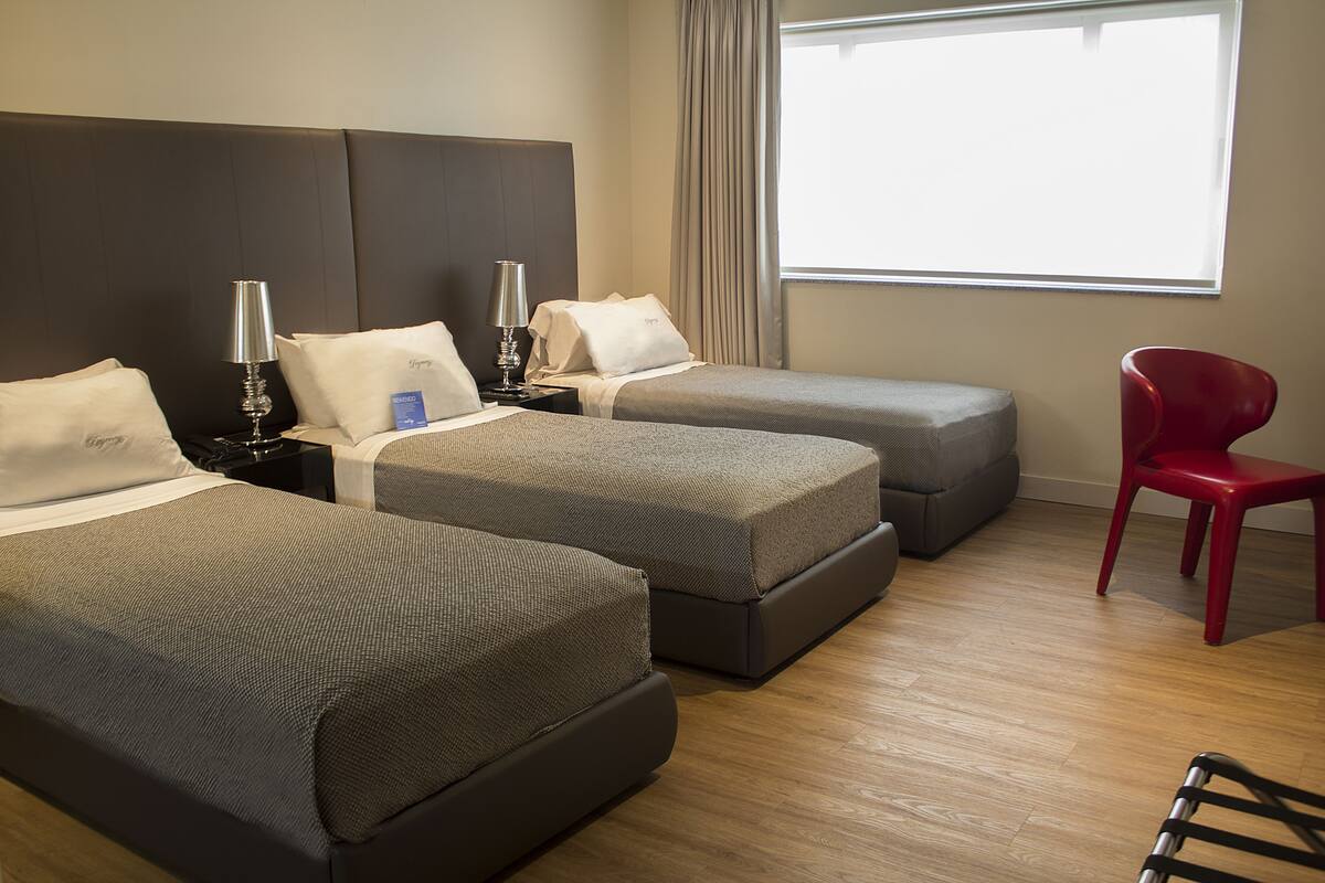 Habitación de hotel con dos camas, una silla roja y un ventanal grande.