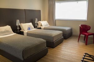 Habitación de hotel con dos camas, una silla roja y un ventanal grande.