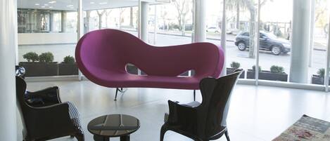 A modern interior with a large window, a purple chair, a small table, and a patterned rug.