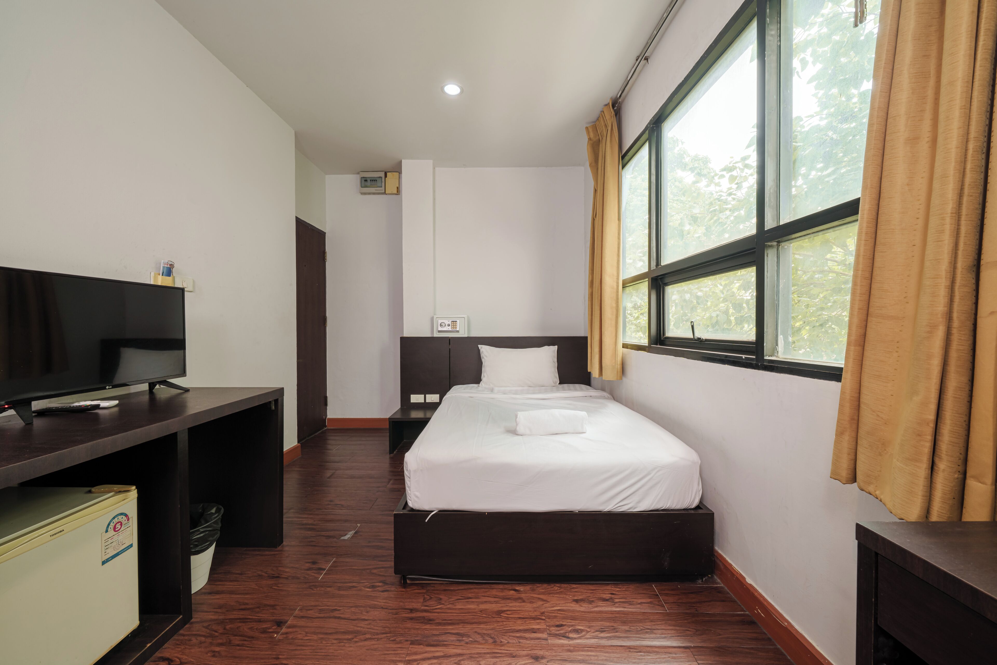 A hotel room with a bed, a desk with a television, and a window with curtains.