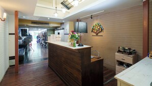 A reception area with a wooden reception desk, a wall-mounted decorative piece, and a ceiling with skylights. - Collection O Khaosan Park (Bangkok)