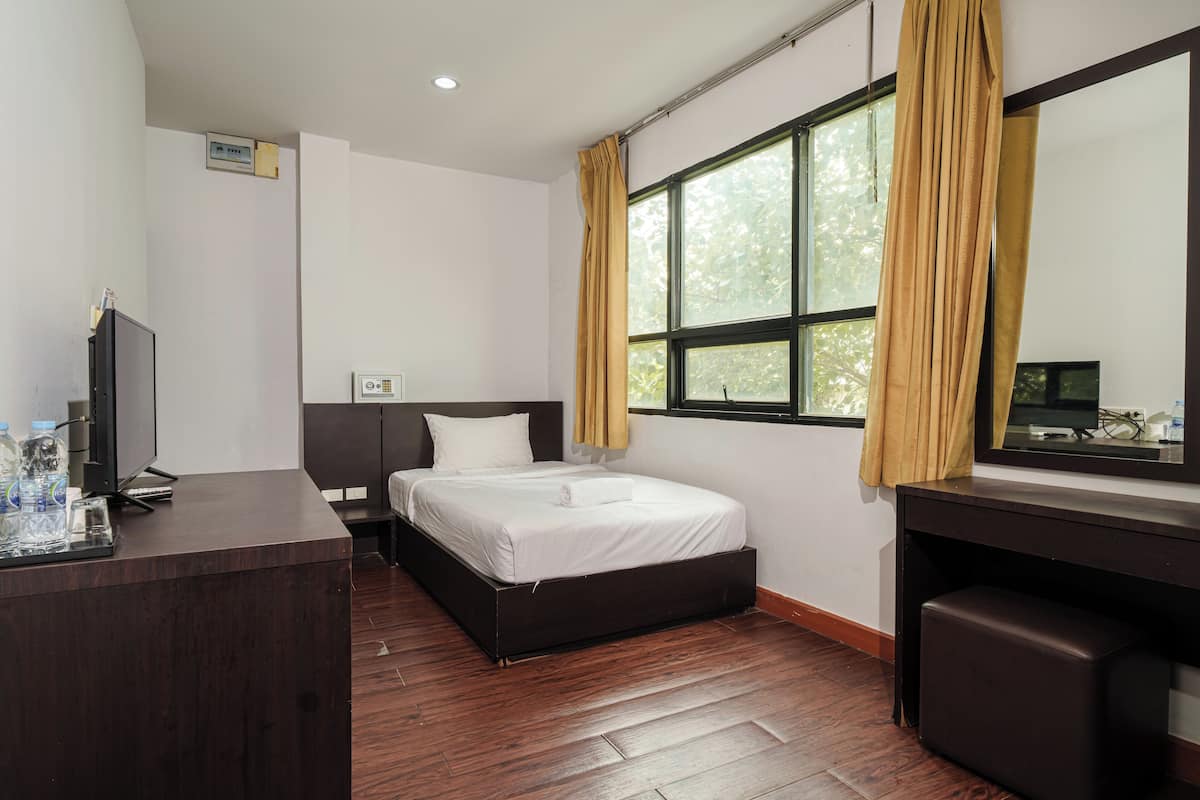 Habitación de hotel con cama, escritorio, televisión y ventana con cortinas.