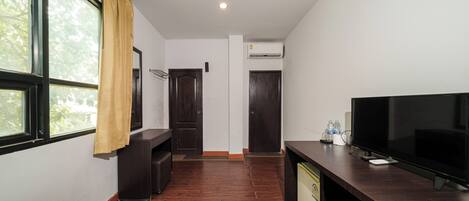 A hotel room with a bed, a TV, a desk, a wardrobe, and a window with curtains.