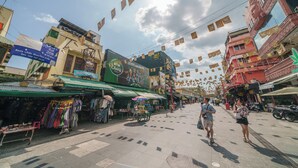 A street with shops and a market stall, a pedestrian crossing, and buildings with signs and banners. - Collection O Khaosan Park (Bangkok)