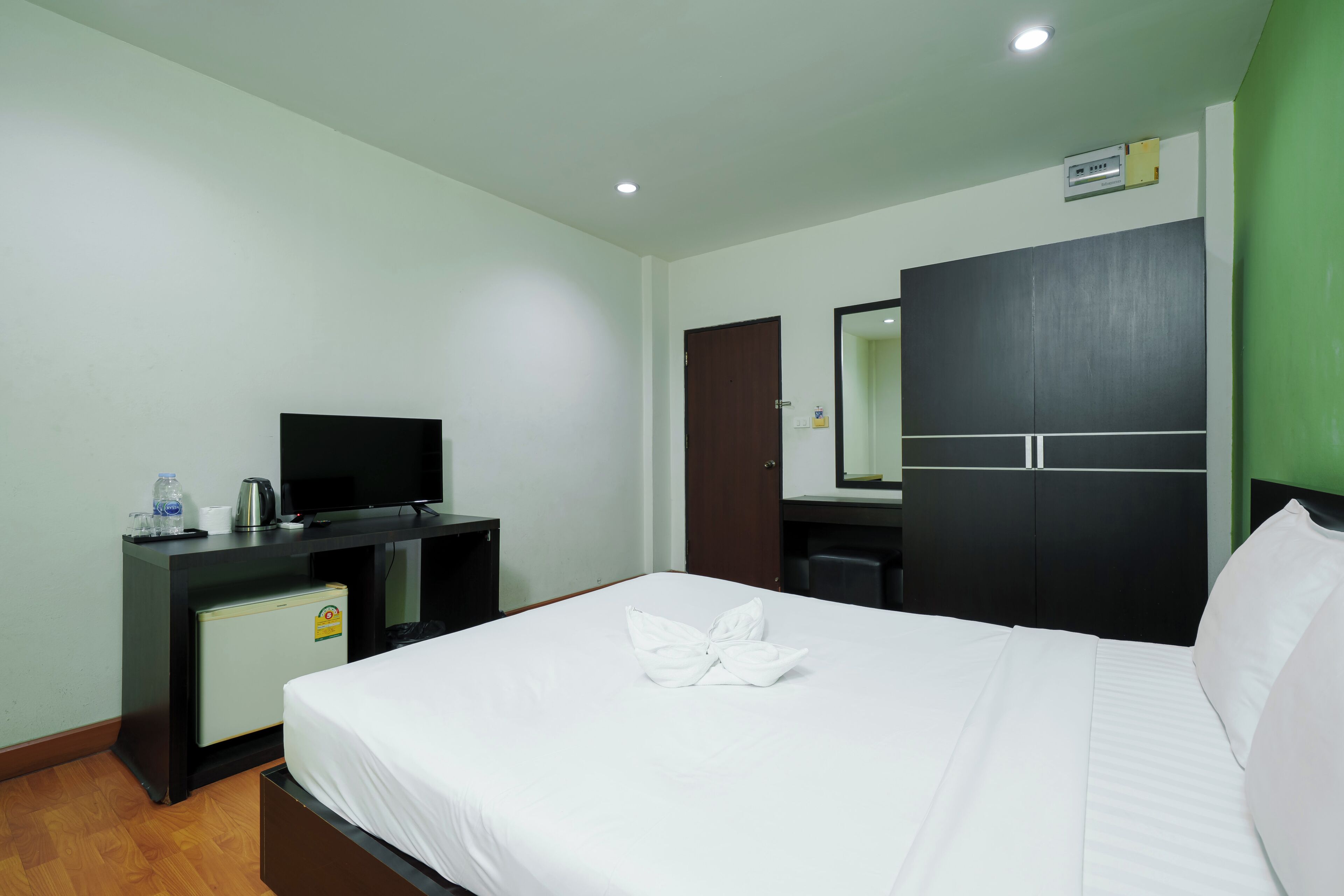 Una habitación de hotel con cama, escritorio, televisor, refrigerador pequeño y armario.