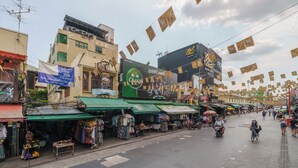 A street market with various stalls and shops, a prominent green awning, and a large billboard advertising a product. - Collection O Khaosan Park (Bangkok)