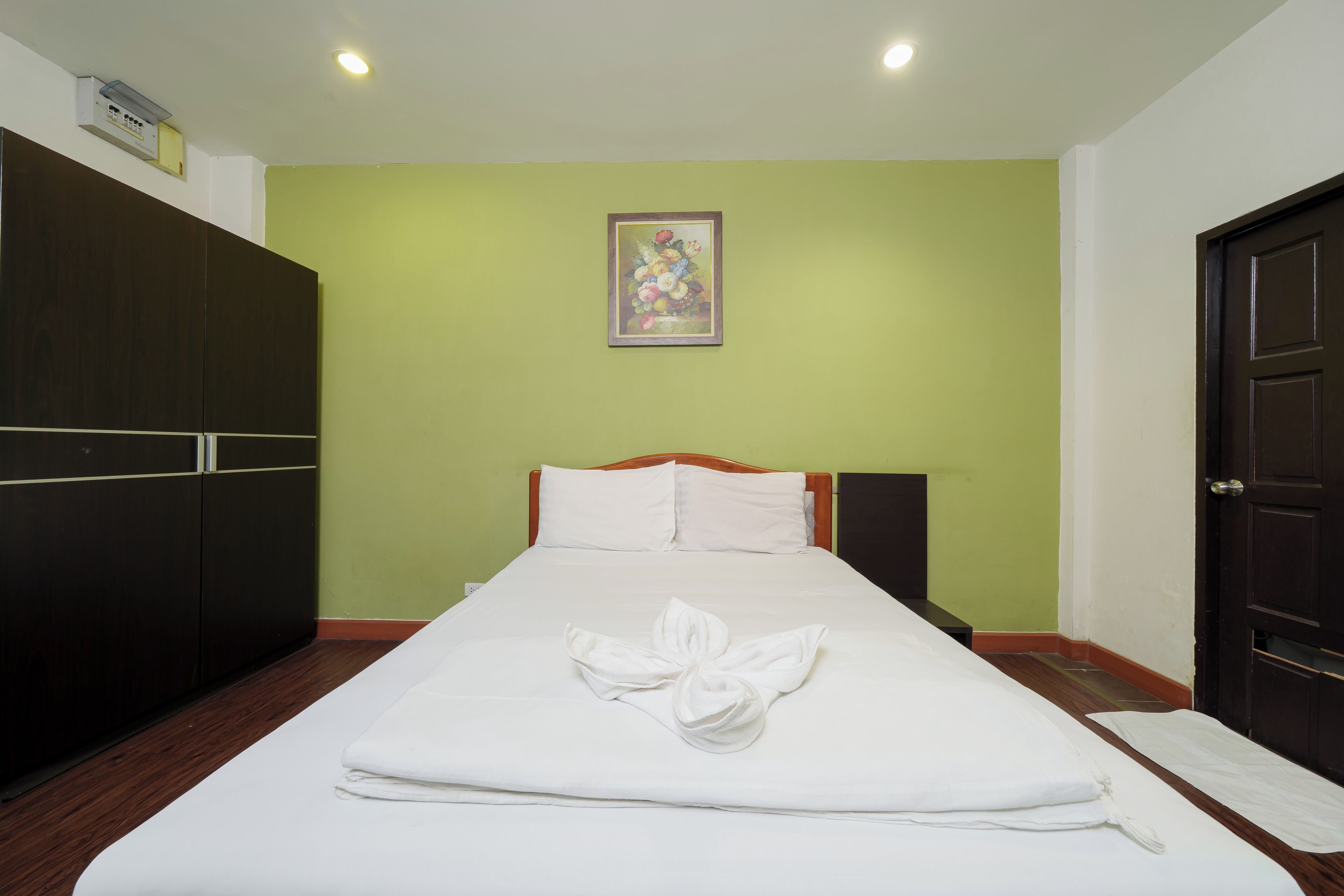 Una cama bien tendida con una disposición de toallas, un armario de madera, un cuadro en la pared y una puerta a la derecha.