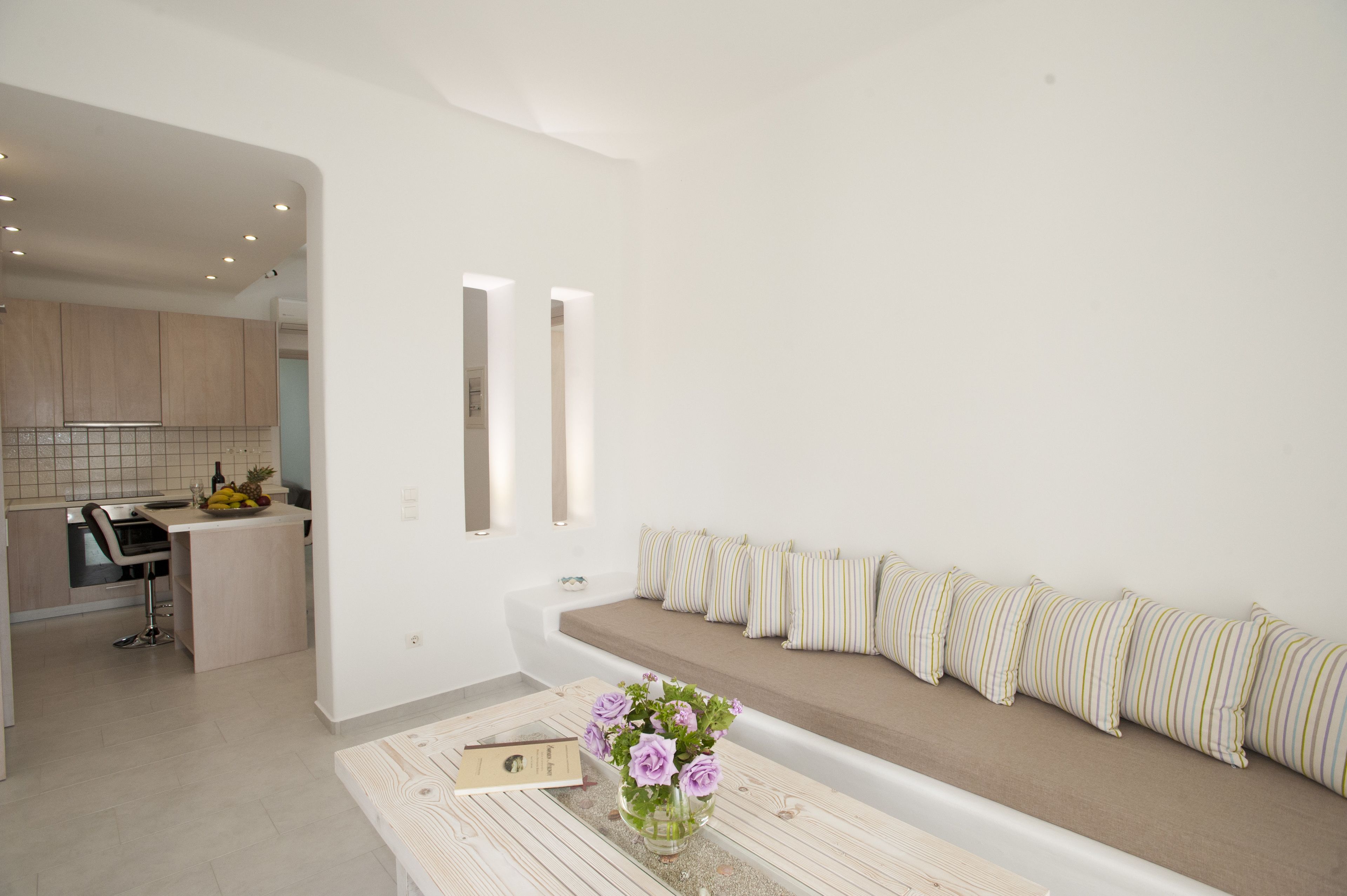 A modern kitchen with a dining area, a bench with striped cushions, and a vase with flowers on a table.