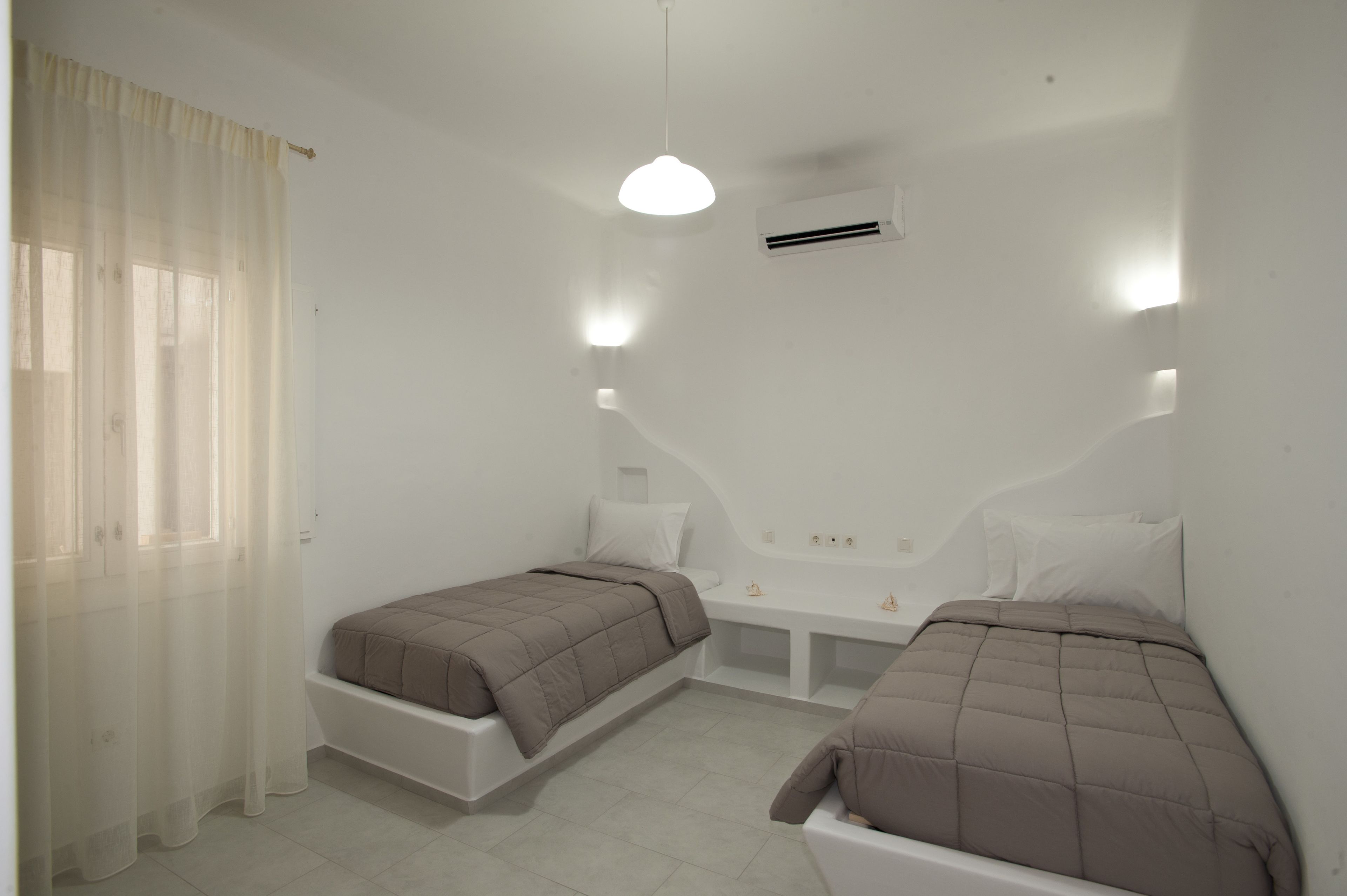 Un dormitorio pequeño y moderno con dos camas, un banco y una lámpara en el techo.