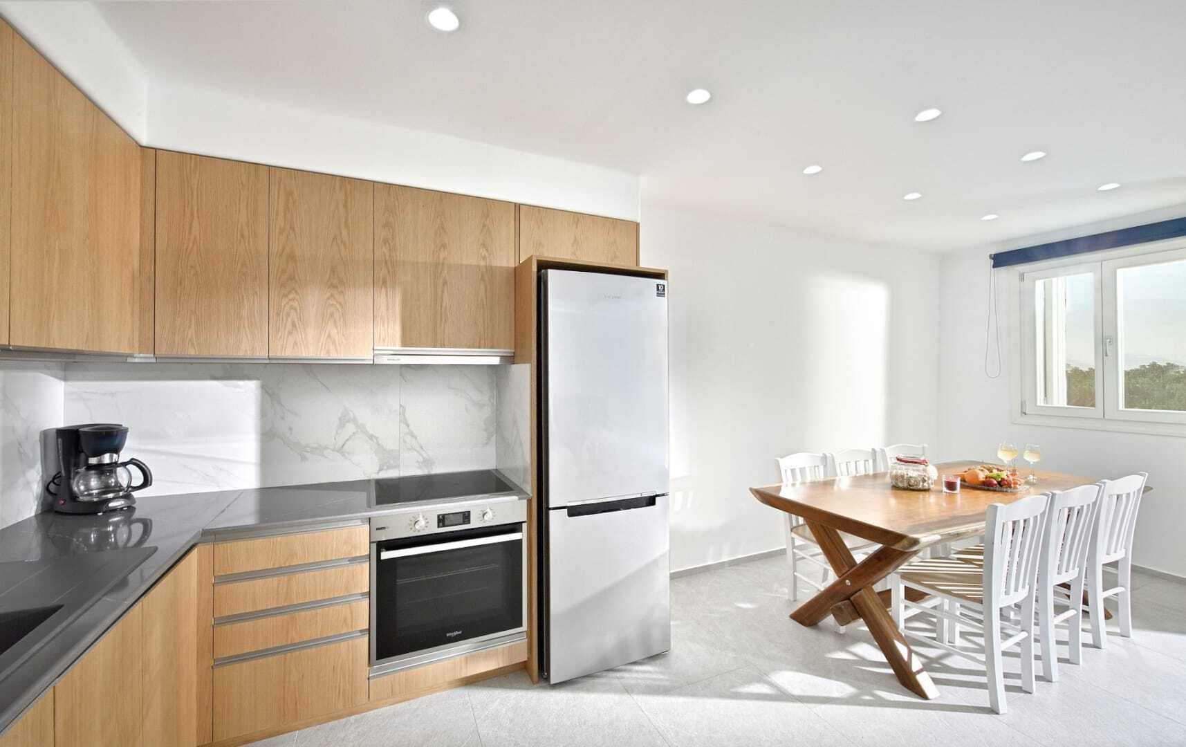 Una cocina moderna con armarios de madera, horno integrado, refrigerador y un comedor con mesa y sillas.