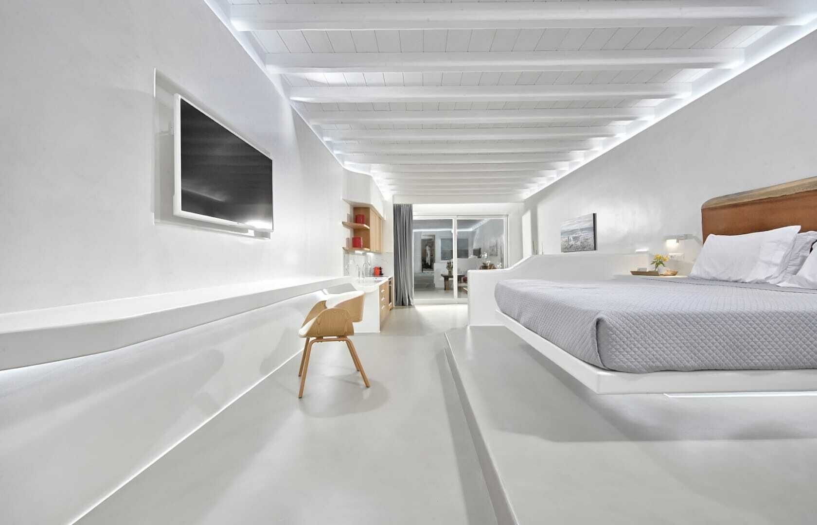 A modern hotel room with a large bed, a desk, and a view into the bathroom.