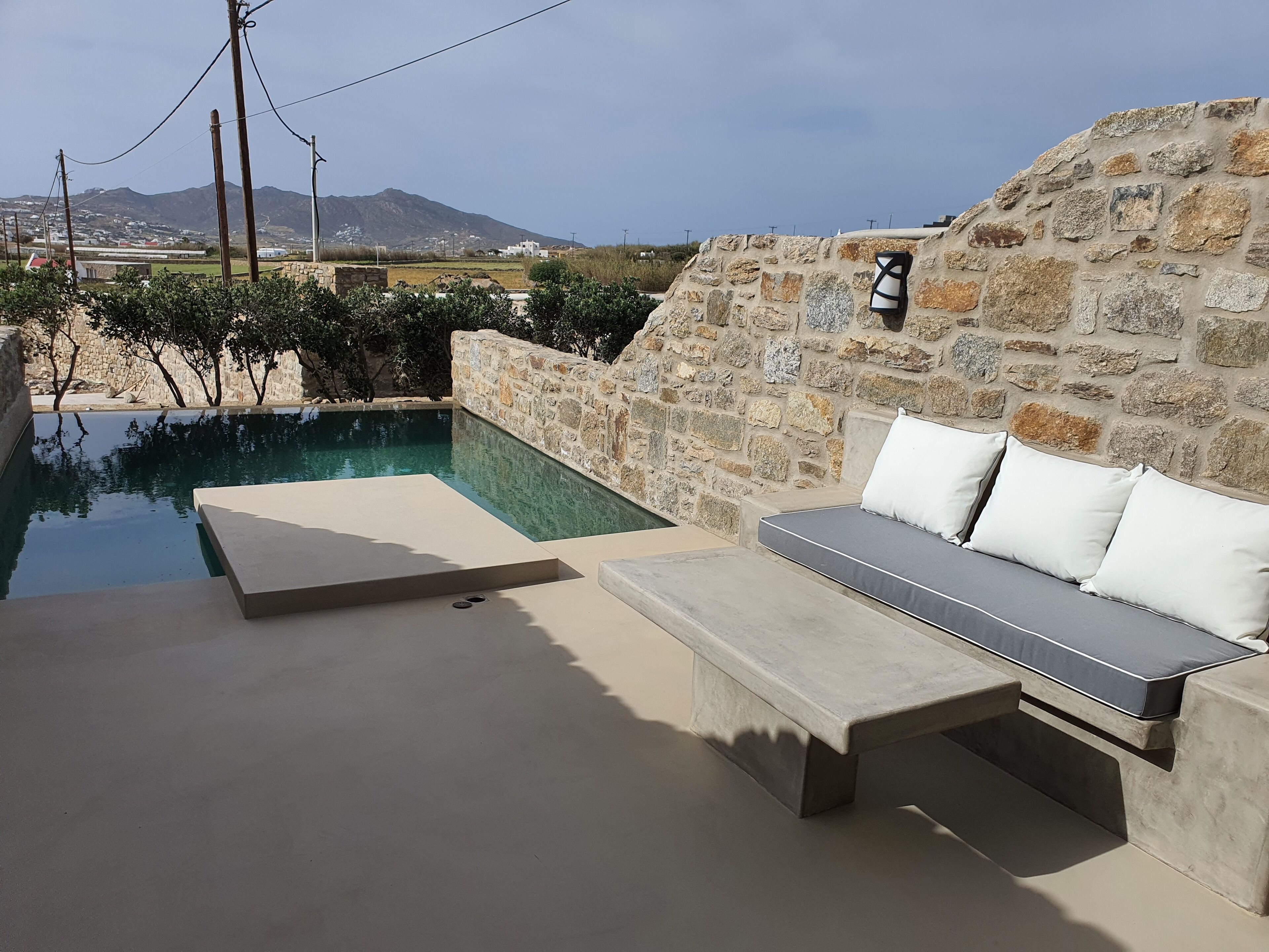 A poolside area with a stone wall, a bench, and a sofa with cushions.