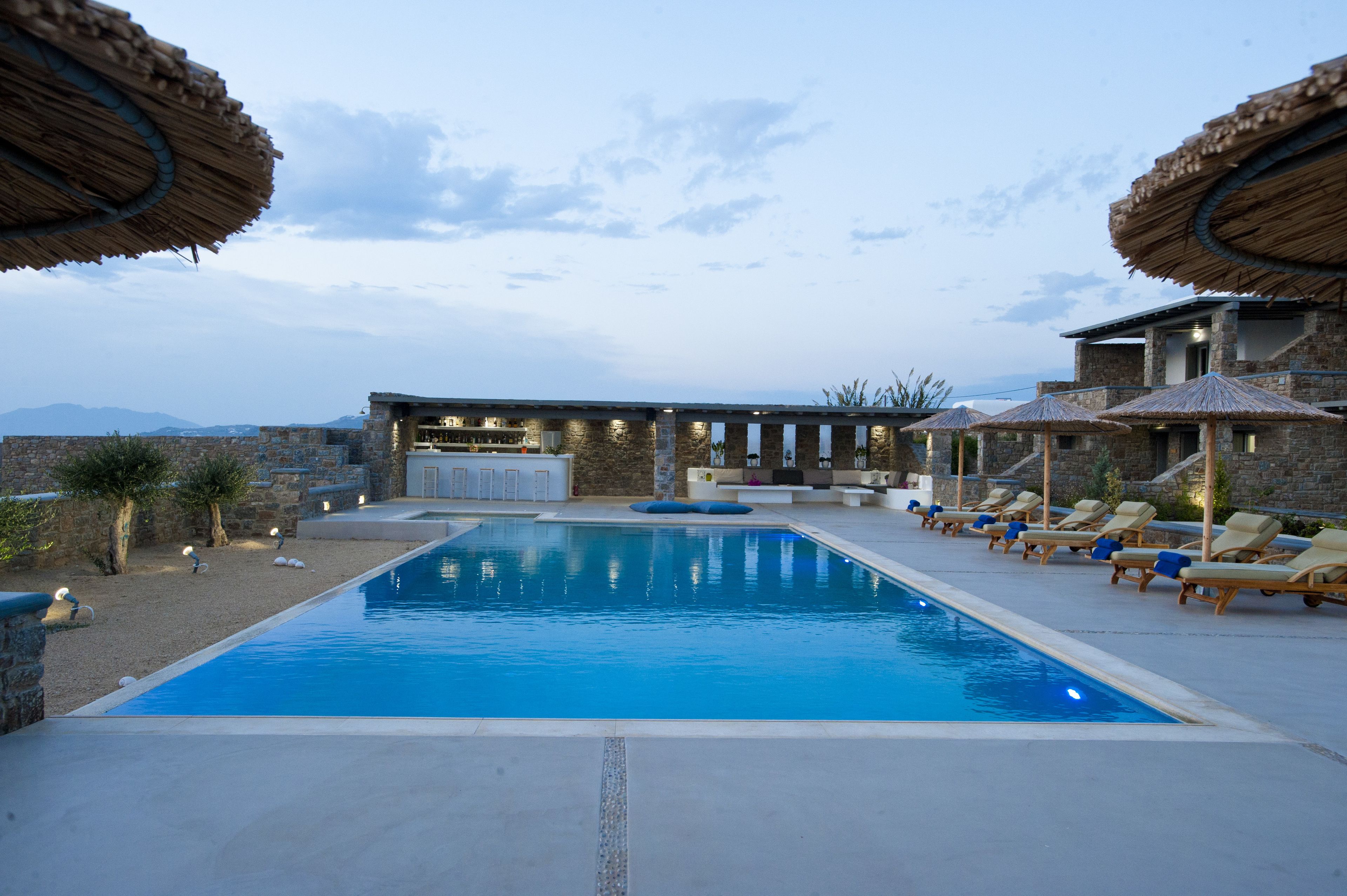 Ein Pool mit Liegestühlen und Sonnenschirmen, umgeben von Steinmauern und einem Barbereich.