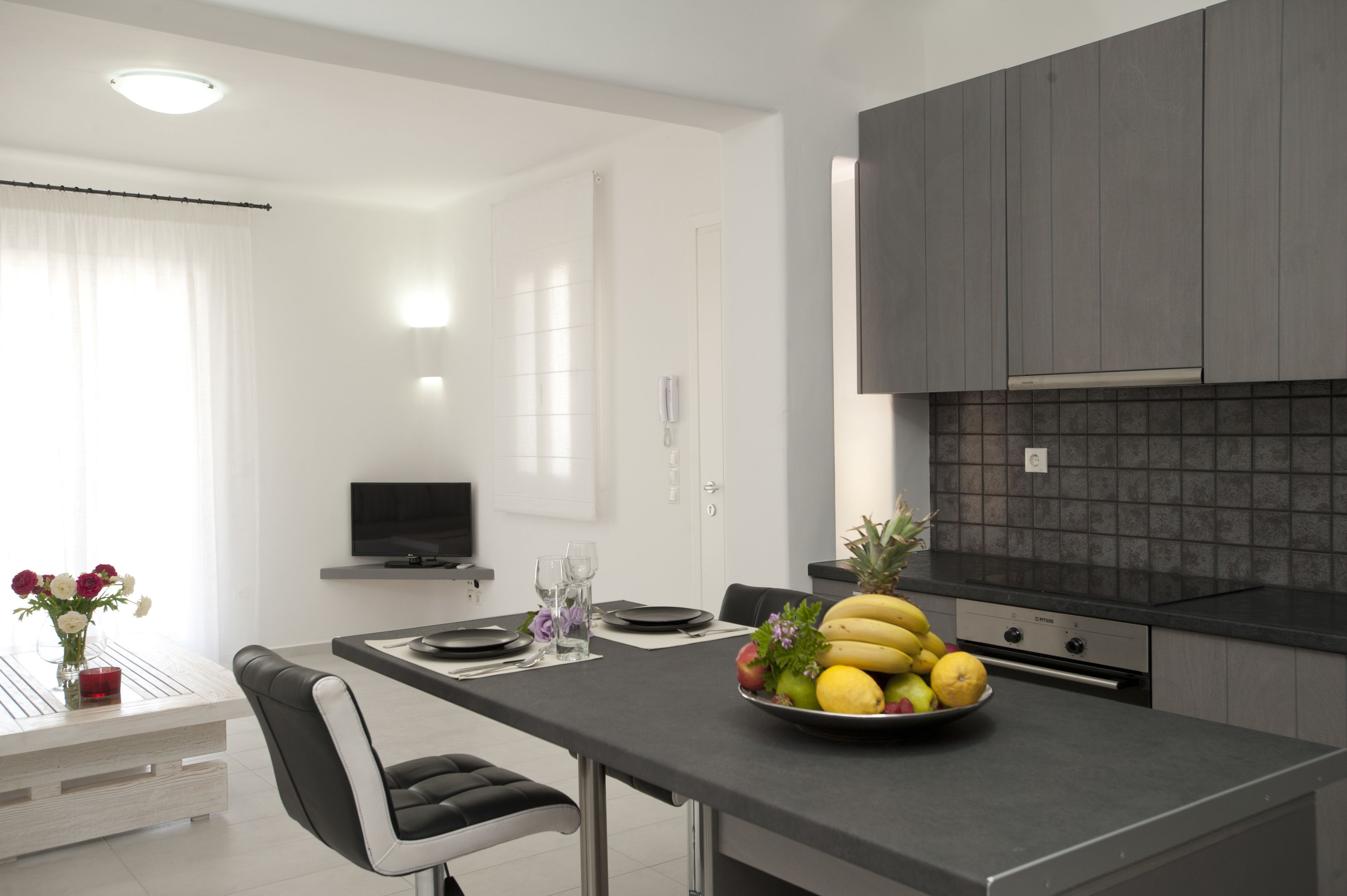 A modern kitchen with grey cabinets, a black countertop, and a fruit bowl on the table.