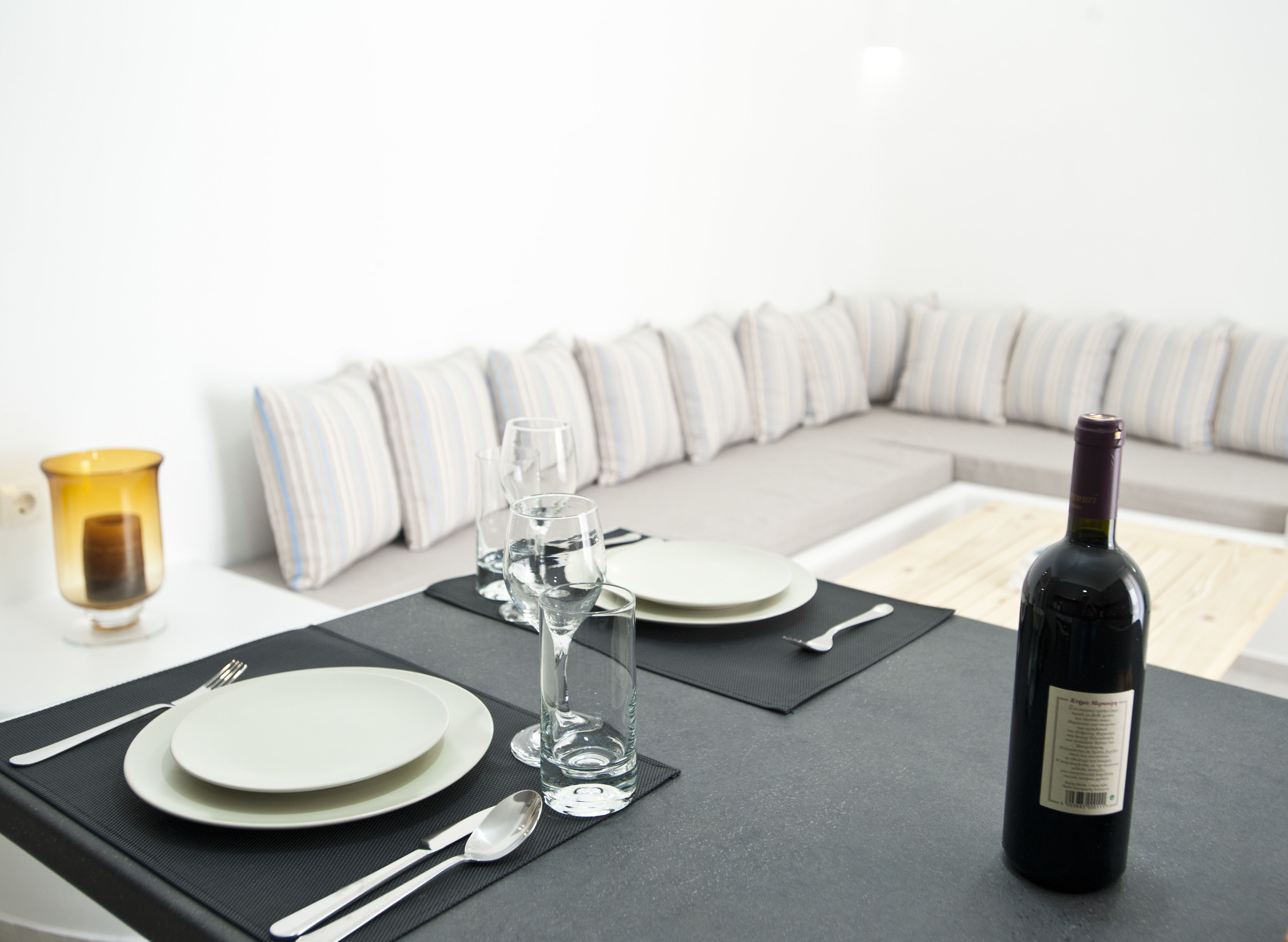 A dining table set with plates, cutlery, glasses, and a bottle of wine, with a sofa in the background.