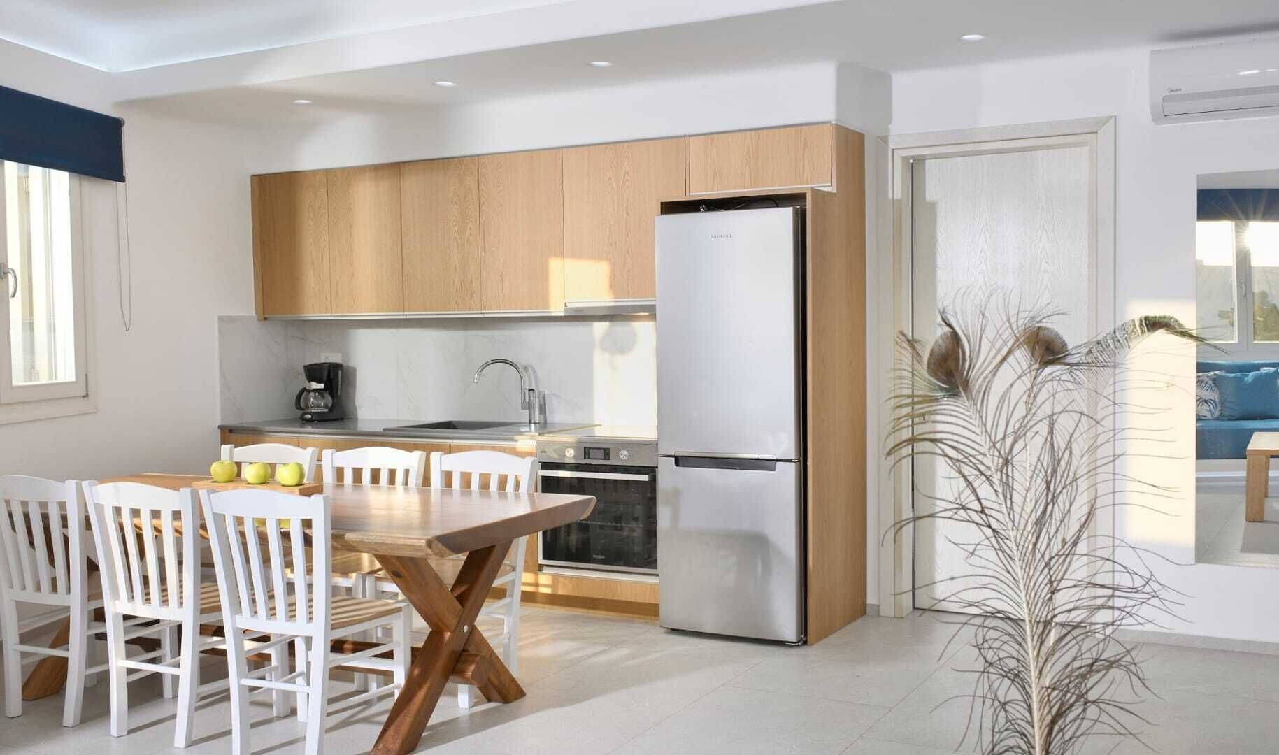 Eine moderne Küche mit Holzschränken, einem Edelstahlkühlschrank, einem Esstisch mit Stühlen und einem großen Fenster.