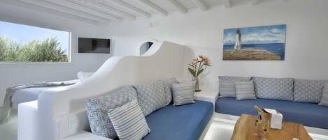 A modern room with a white sofa set, a wooden coffee table with drinks, and a painting of a lighthouse.