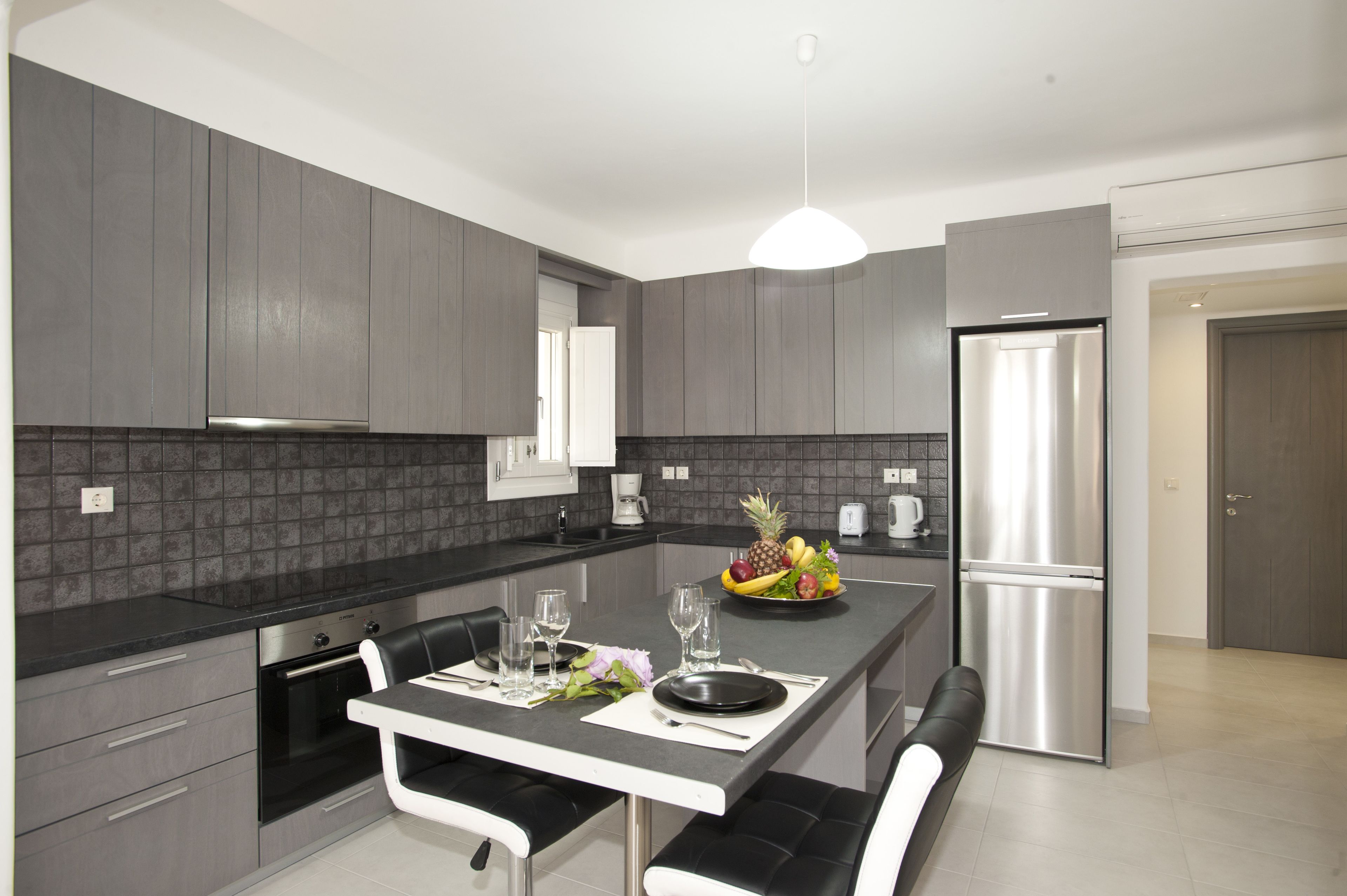 A modern kitchen with grey cabinetry, a stainless steel refrigerator, and a dining area with a black and white table set.
