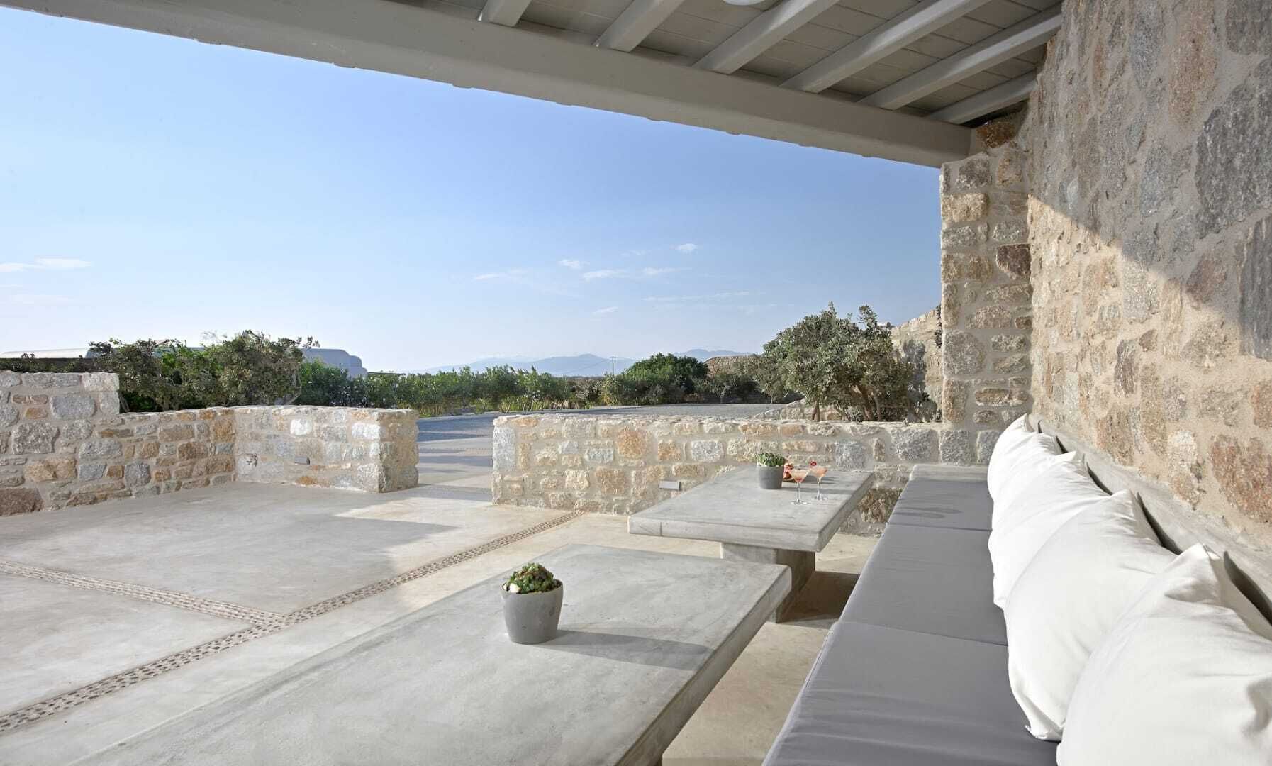 A rooftop terrace with stone walls, a seating area, and a view of the landscape.