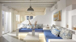A modern living room with a blue sofa, white furniture, and a painting on the wall. - AC Village Christoulis (Mykonos)