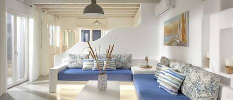 A modern living room with a blue sofa, white furniture, and a painting on the wall.