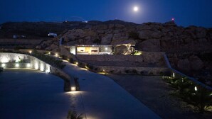 Un bâtiment moderne, auquel mène un chemin pavé de pierres, entouré d’un paysage rocheux et surplombant un ciel nocturne dégagé.