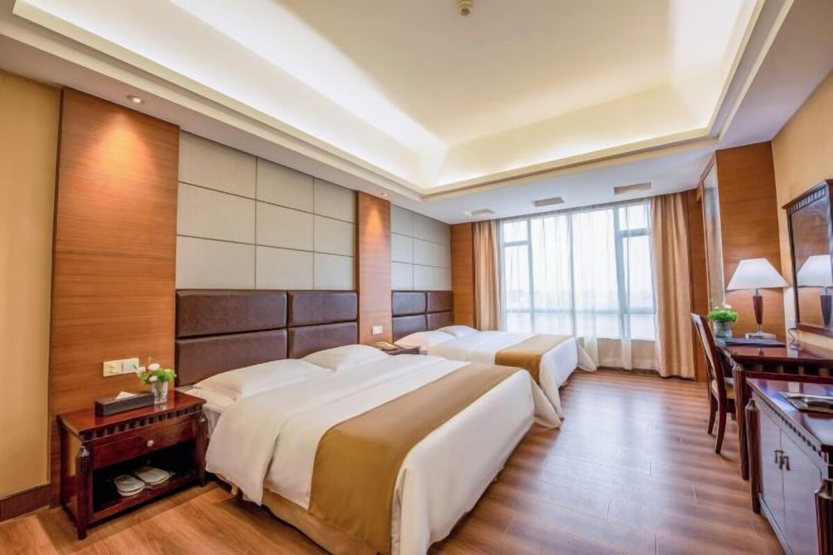 A hotel room with two beds, a desk, and a large window.