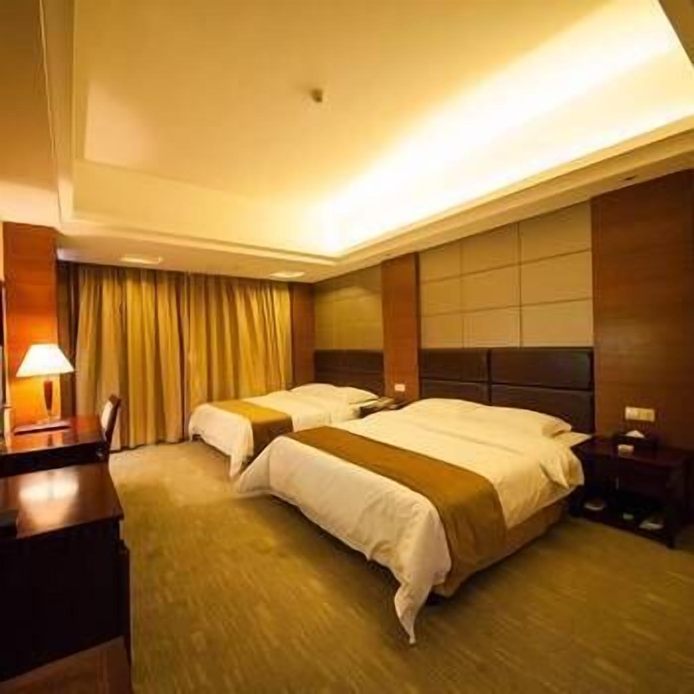 A hotel room with two beds, a desk, and a lamp.