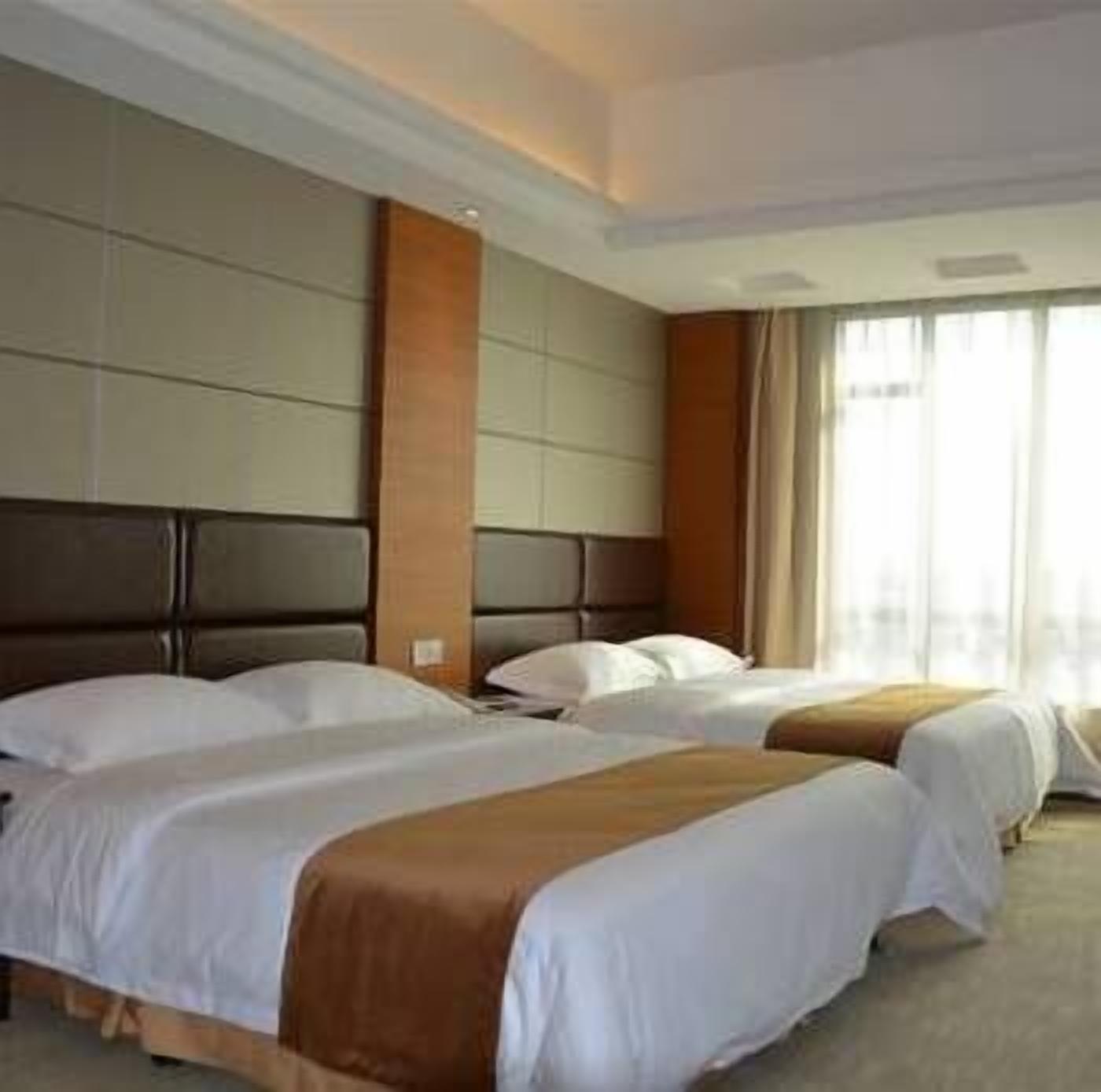Habitación de hotel con dos camas, un ventanal con cortinas y un cabecero moderno.