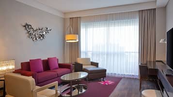 Ein modernes Hotelzimmer mit einem roten Sofa, einem beigen Sessel, einem runden Couchtisch und einem Flachbildfernseher.