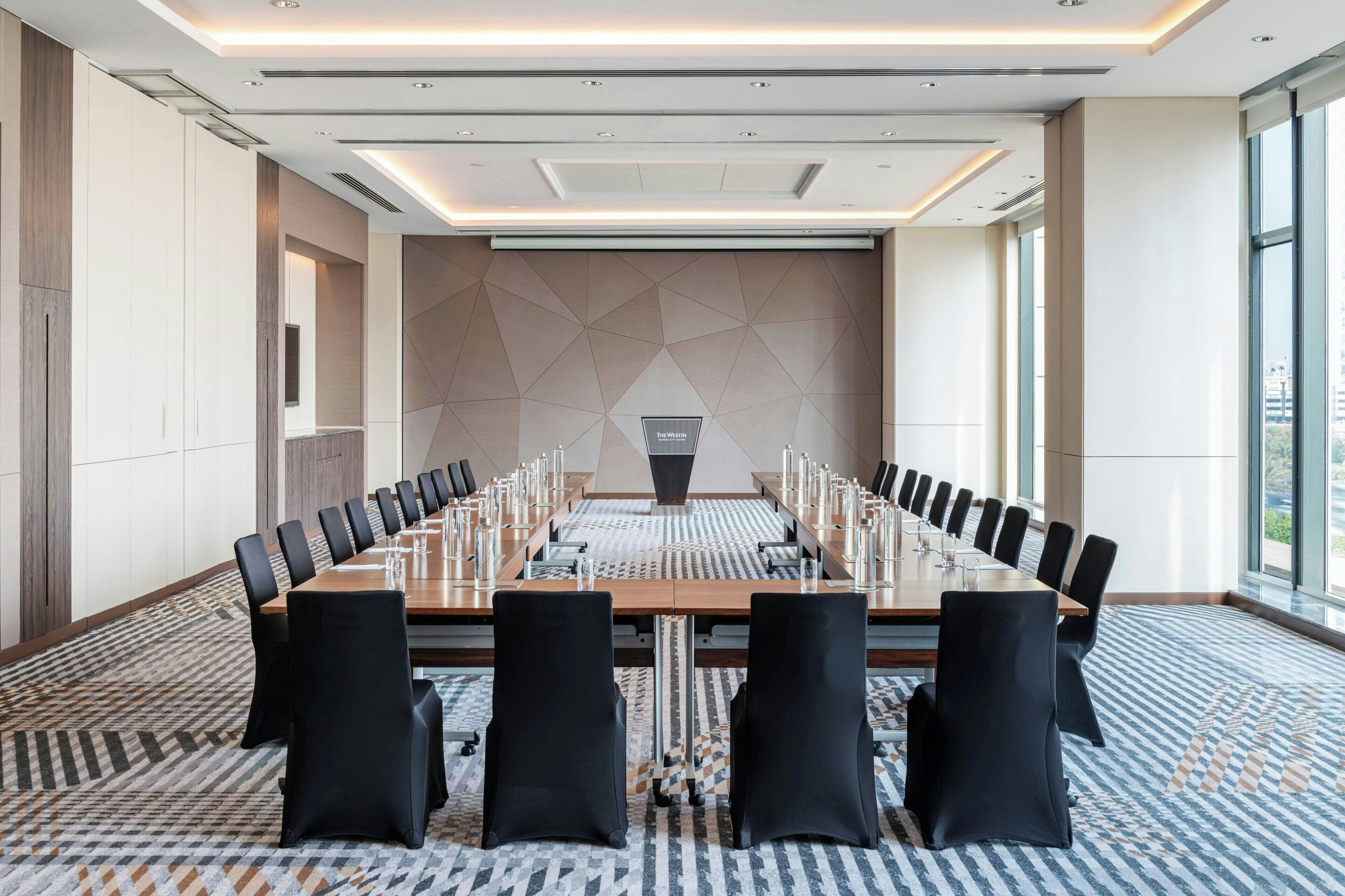 A conference room with a long table, black chairs, and a patterned carpet.