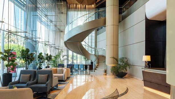 Un vestíbulo amplio con una escalera curva, asientos cómodos y ventanas grandes.