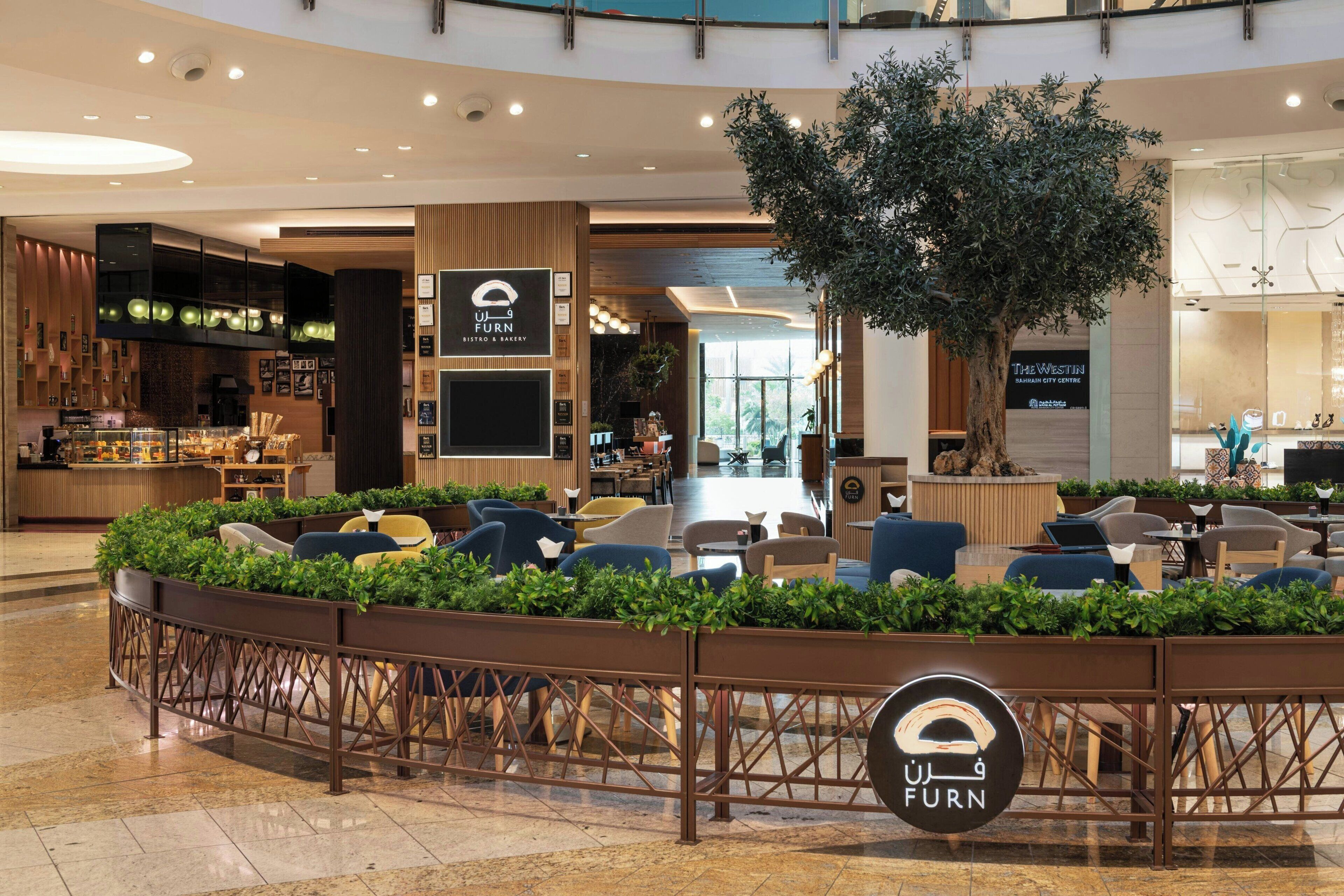 A modern furniture store with a central seating area surrounded by greenery, a large tree, and a sign reading "FURN".