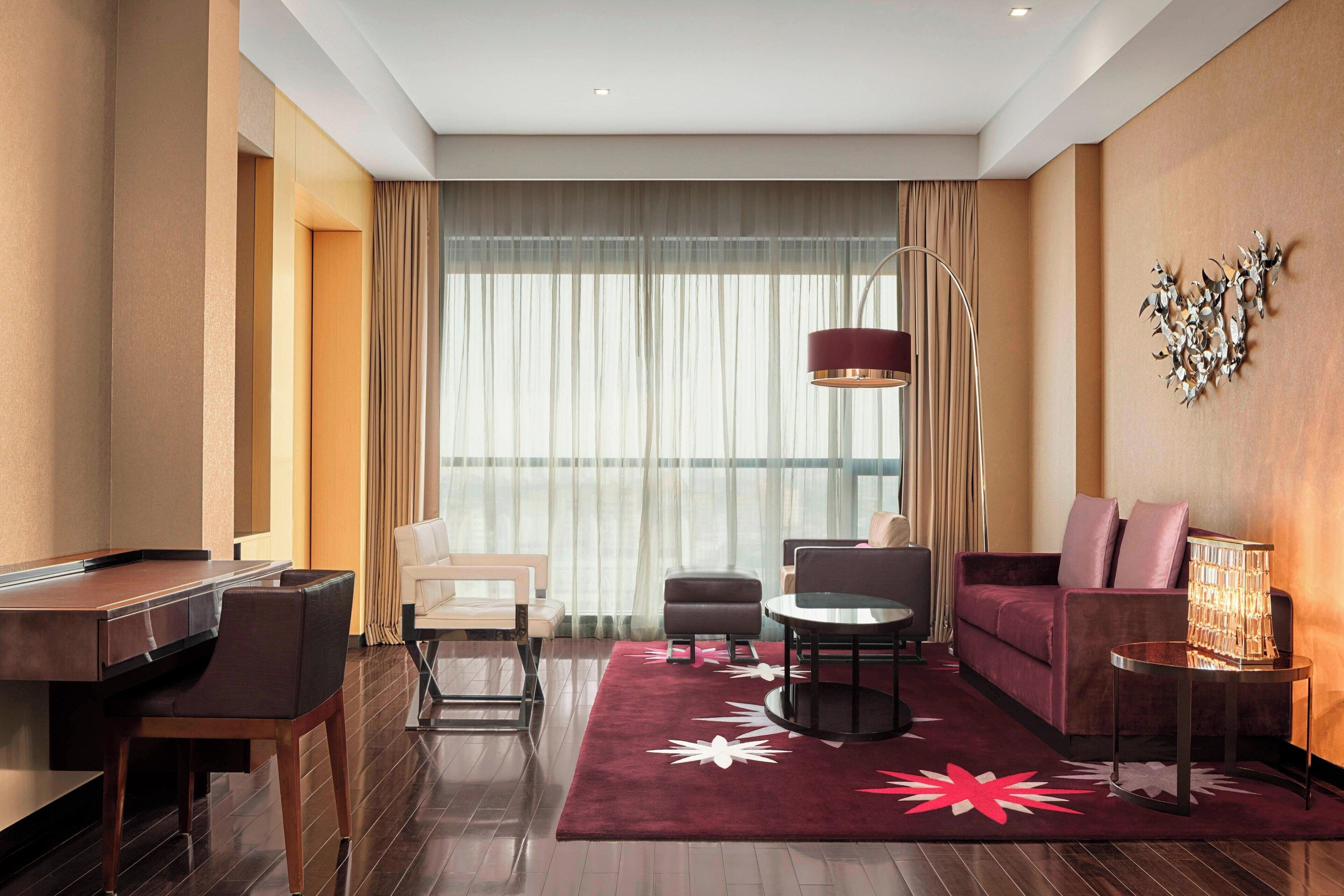 Een moderne hotelkamer met een bureau, een bank en een groot raam met gordijnen.