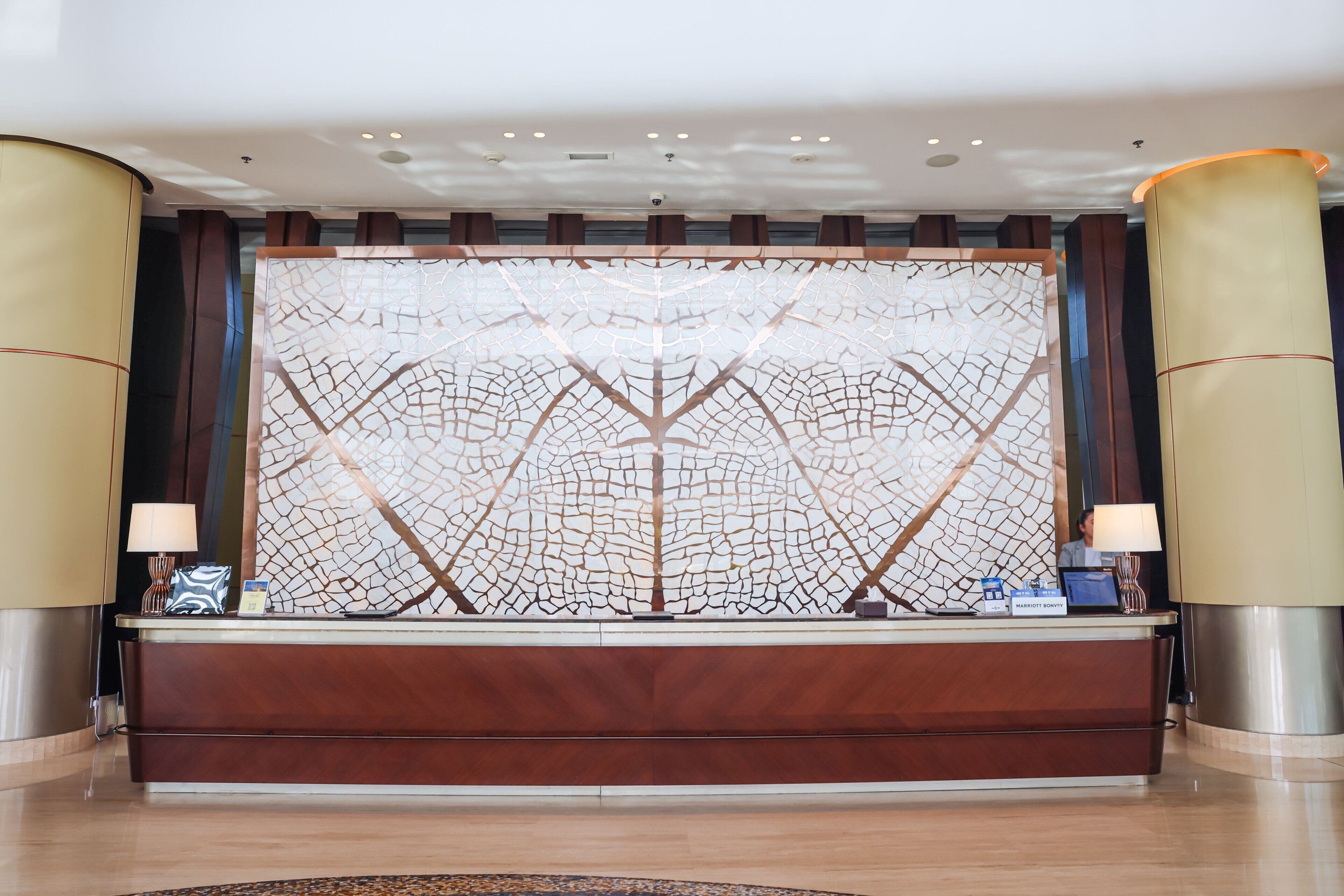 A reception area with a wooden reception desk, a decorative wall with a geometric pattern, and two lamps on either side.