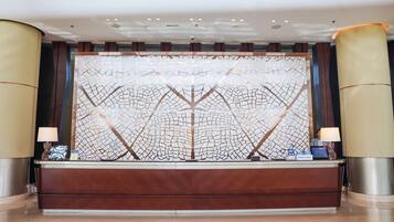 A reception area with a wooden reception desk, a decorative wall with a geometric pattern, and two lamps on either side.