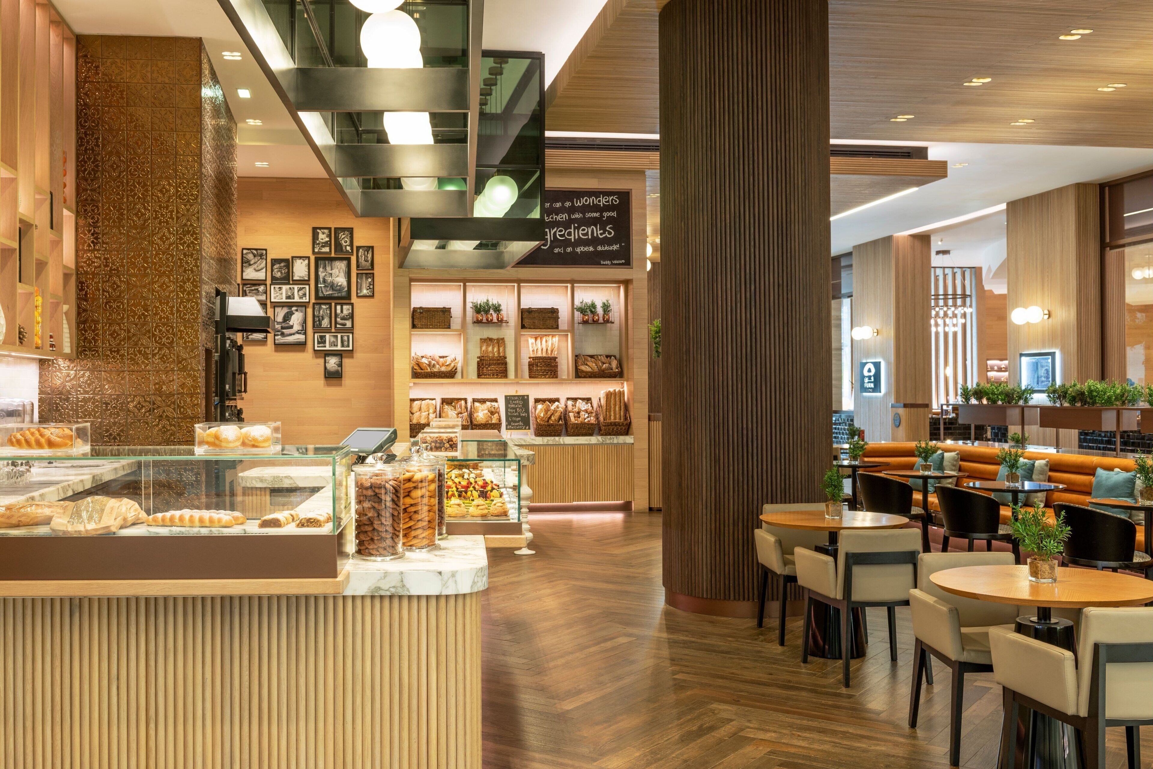 A modern cafe with a wooden interior, a counter displaying pastries, and seating areas with tables and chairs.
