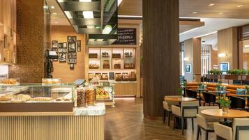 A modern cafe with a wooden interior, a counter displaying pastries, and seating areas with tables and chairs.
