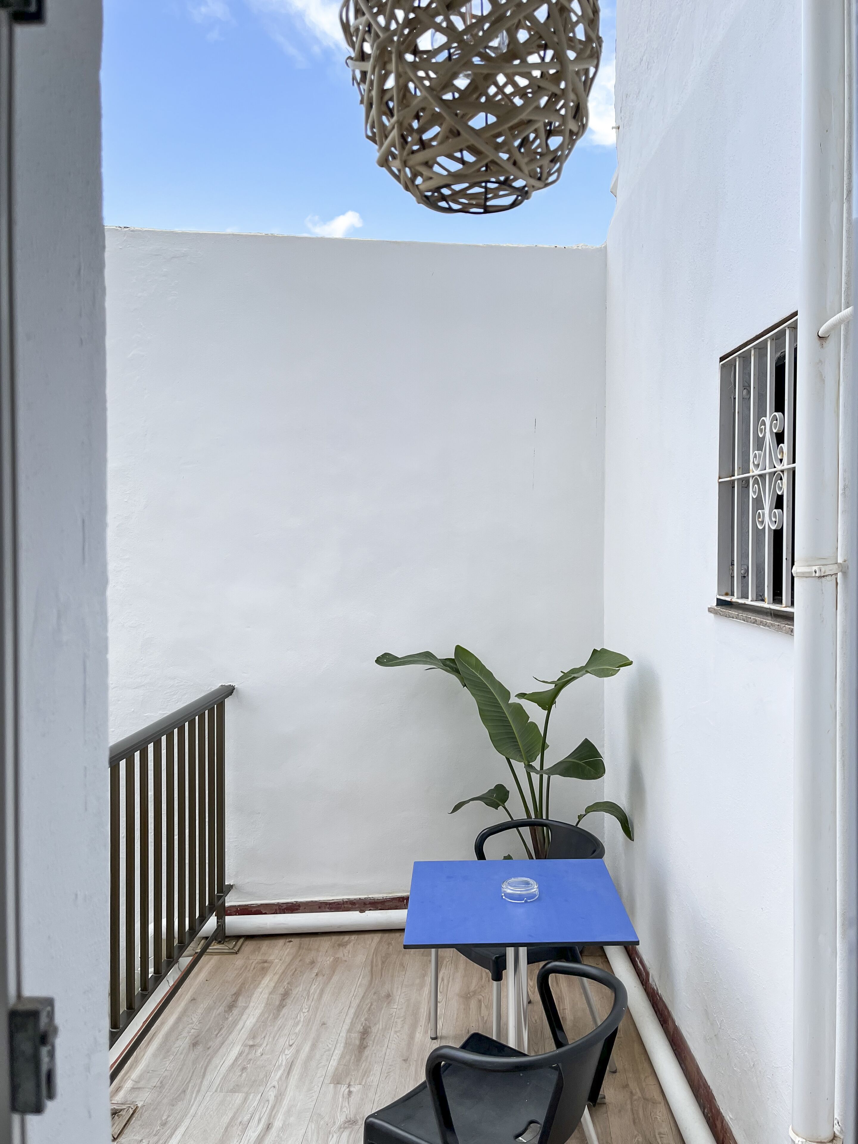 A small outdoor patio with a blue table, a potted plant, and a wicker hanging light fixture.