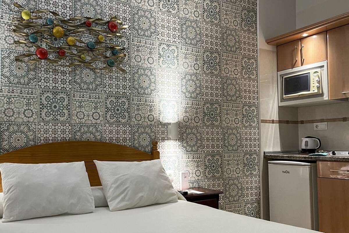 Ein Hotelzimmer mit Bett, Nachttisch, Mikrowelle, Kühlschrank und einer Wand mit dekorativen Fliesen.