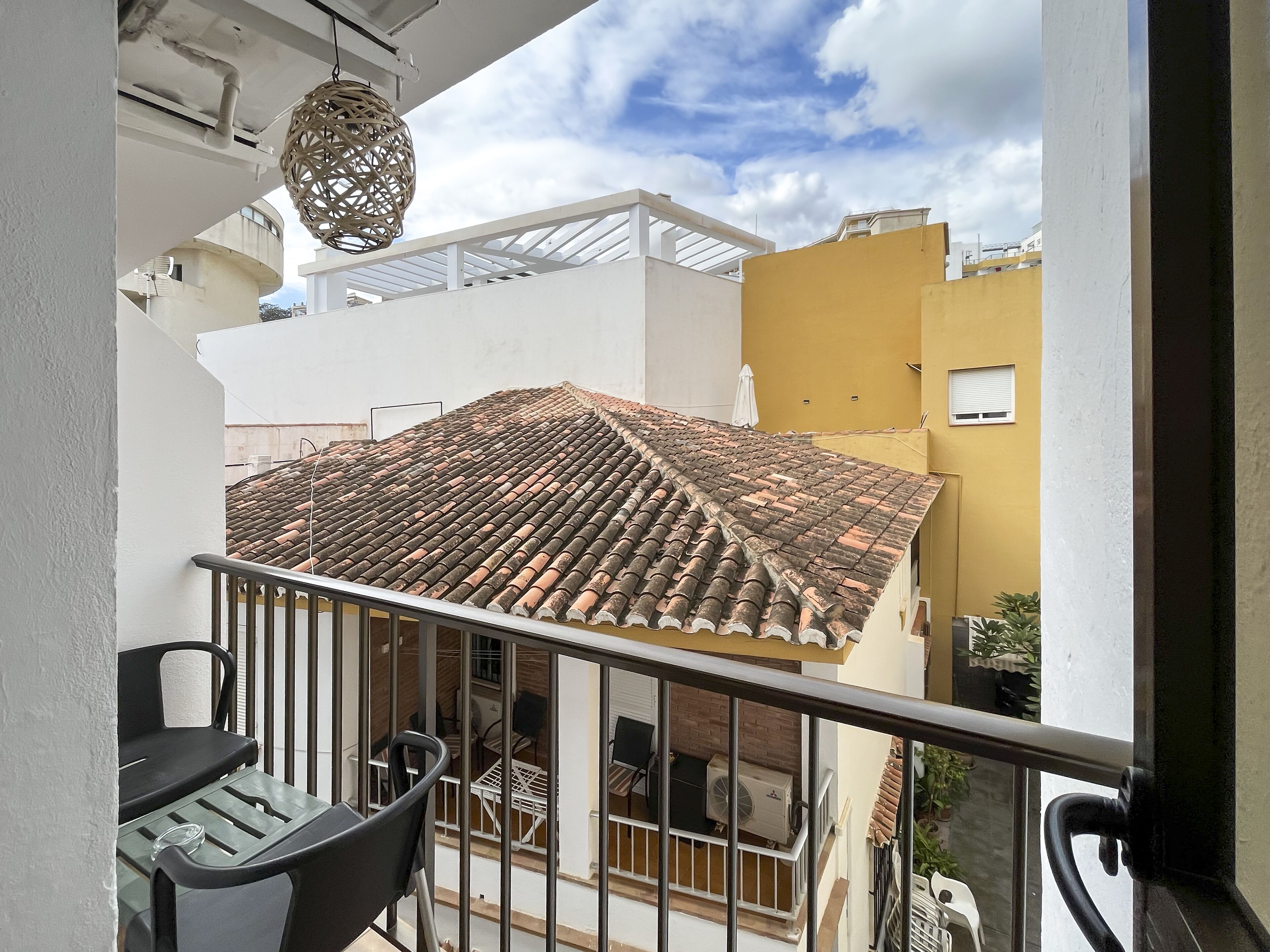 A balcony with a tiled roof, a hanging light fixture, and a view of neighboring buildings.