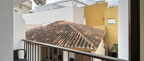 A balcony with a tiled roof, a hanging light fixture, and a view of neighboring buildings.