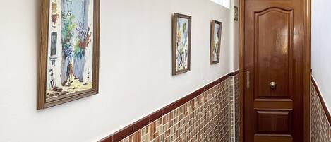 A hallway with tiled walls, a wooden door with the number 234, and three framed paintings.