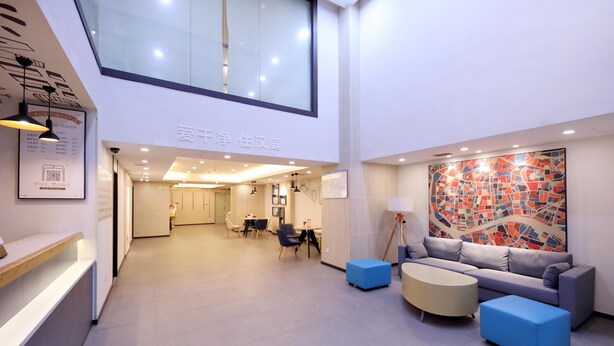 Un moderno vestíbulo de hotel con una recepción, una zona de estar con sofás y otomanas, un comedor y una gran obra de arte abstracta en la pared.
