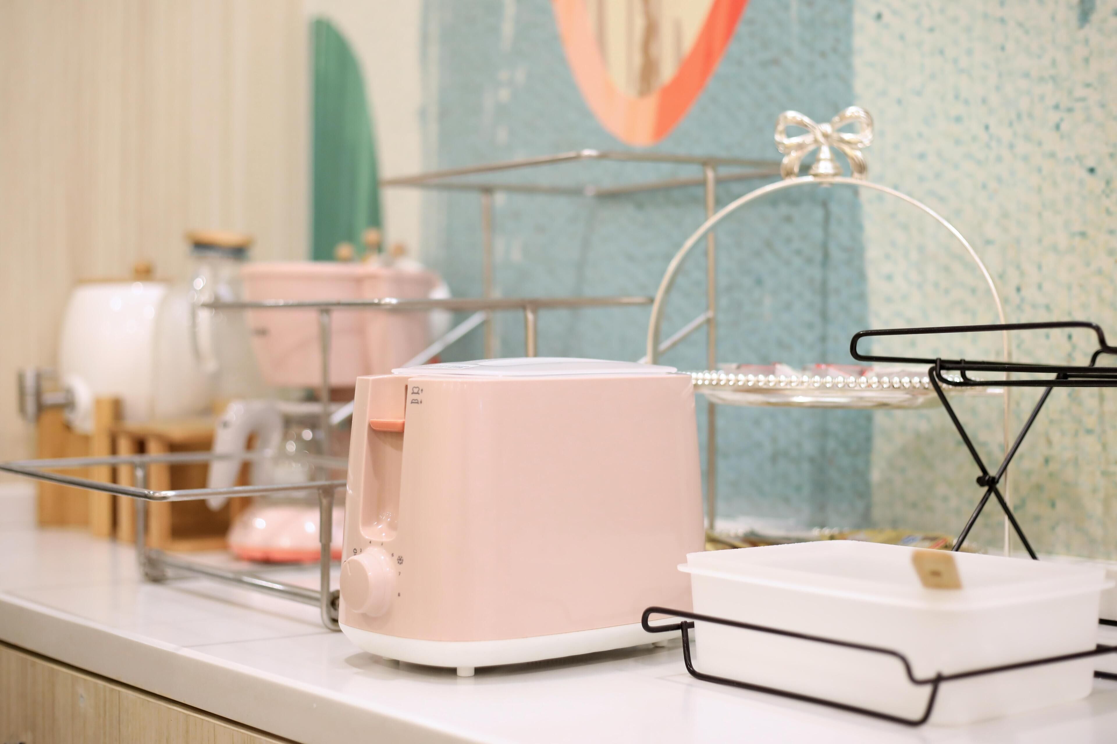 A kitchen counter with a pink appliance, a glass container, and a metal rack with a bow.