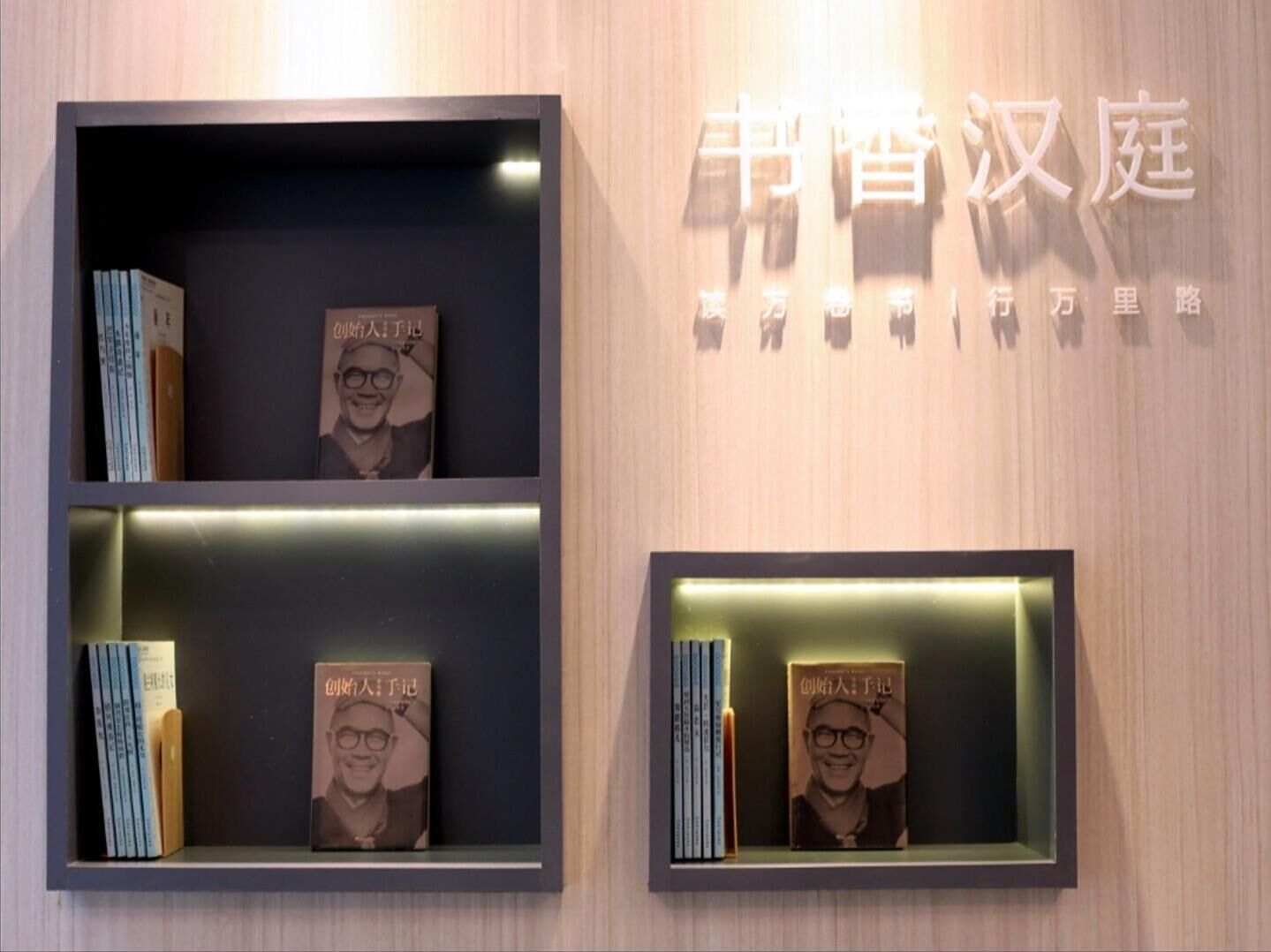 Zwei an der Wand befestigte Vitrinen mit Büchern und einem gerahmten Foto.