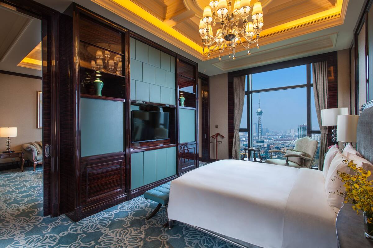 Une chambre d’hôtel spacieuse, dotée d’un grand lit, d’une télévision, d’un coin salon avec vue sur la ville et d’un lustre.